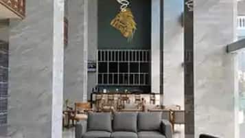 A spacious lobby with a modern grey sofa set, two black round tables, and a chandelier.