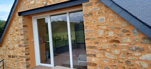 Een gebouw van steen met een grote glazen deur die uitkomt op een buitengebied met een houten terras en een stoel.