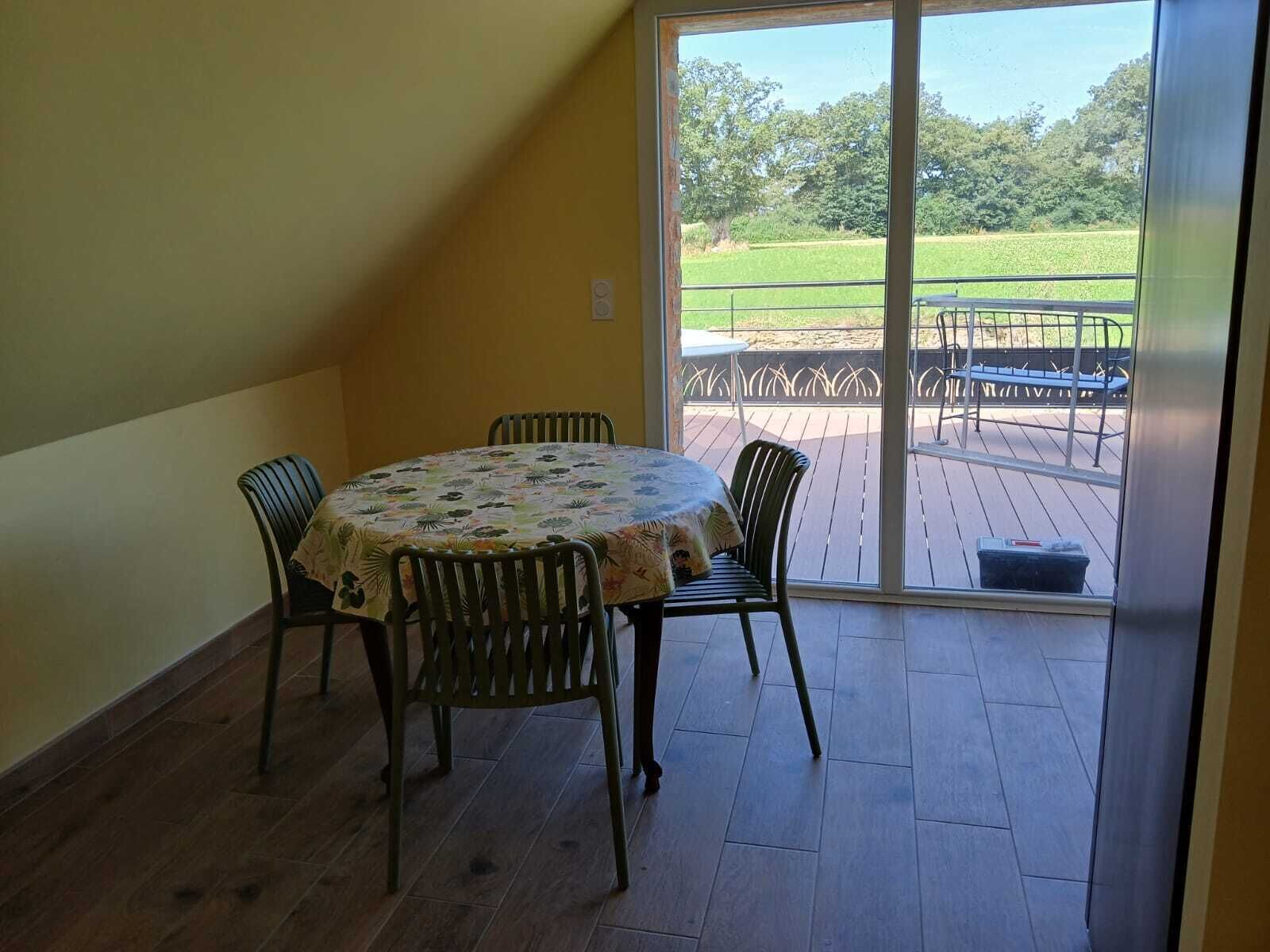 A room with a round table and four chairs, a sliding glass door leading to an outdoor deck with a metal railing.