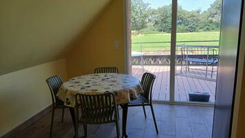 A room with a round table and four chairs, a sliding glass door leading to an outdoor deck with a metal railing.