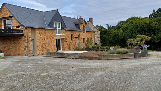 A stone building with a balcony, a gravel driveway, and a garden with potted plants. - Logis de la Provosterie - CROCUS (Ahuille)
