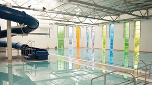 Une piscine intérieure dotée d’un toboggan bleu, de murs en verre et d’une structure de toit en métal.