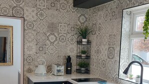 Une cuisine moderne avec des meubles de couleur sombre, un plan de travail blanc et un revêtement mural à motifs.