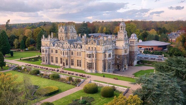Un grand bâtiment historique à la façade symétrique, doté de nombreuses tours et agrémenté d’un jardin bien entretenu, avec des allées et des haies.