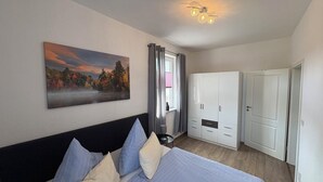 Een slaapkamer met een bed, een kledingkast, een schilderij en een plafondlamp.