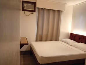 A hotel room with a bed, a nightstand, a wall-mounted air conditioner, and a window with curtains. - Dormitels.ph - El Nido (El Nido)