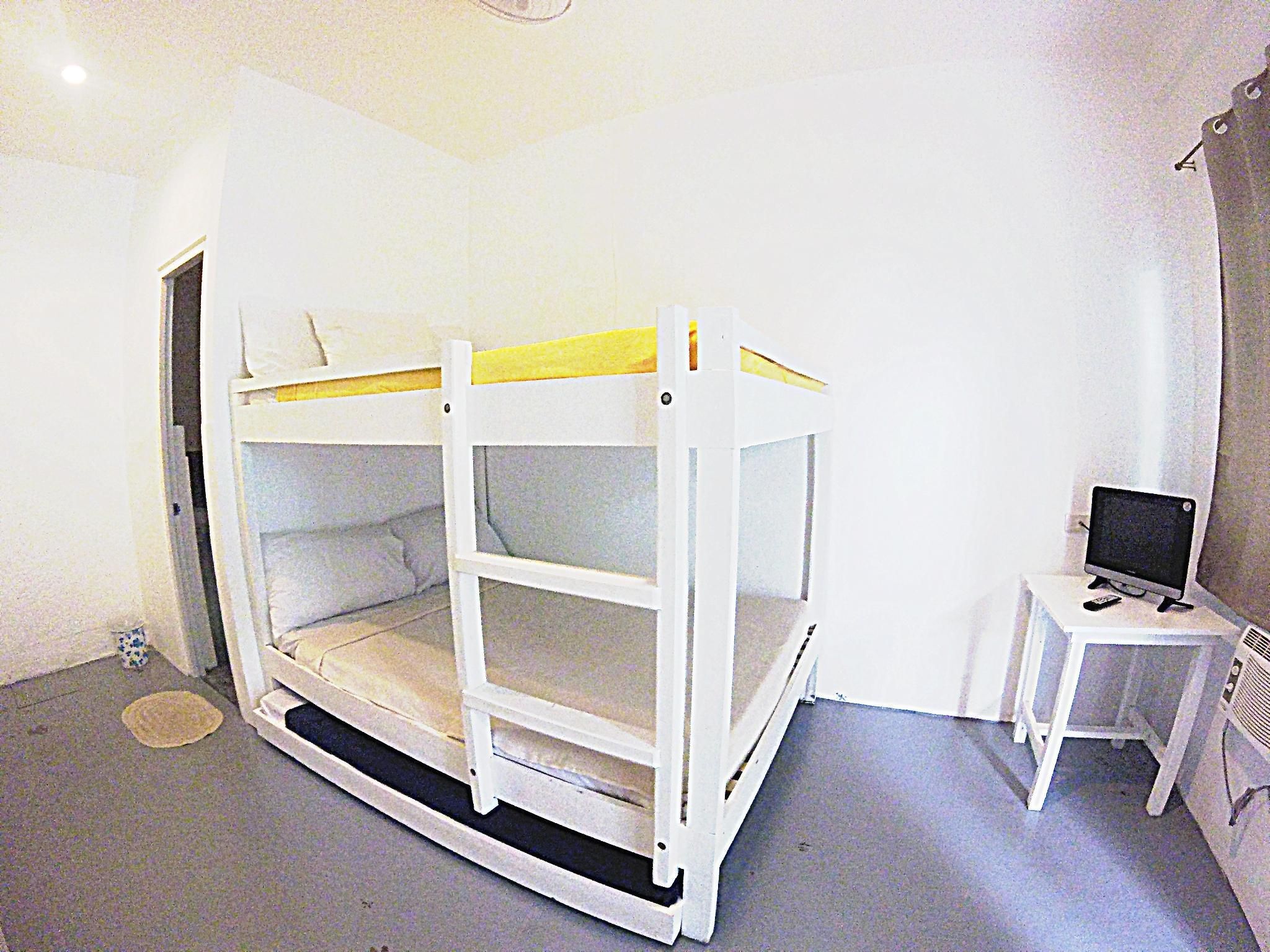 A room with a bunk bed, a small desk with a computer, and a window.