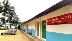 Il s’agit d’un bâtiment sur lequel on peut lire les inscriptions « Dormitels.ph » et « EL NIDO », ce qui indique qu’il s’agit d’une auberge de jeunesse. On y voit des lits superposés à l’extérieur, un palmier et une petite construction qui ressemble à une cabane.