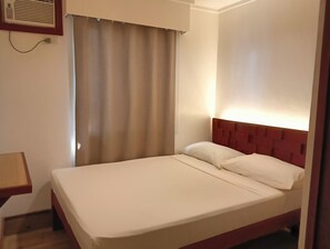 A hotel room with a single bed, a wooden nightstand, a wall-mounted air conditioning unit, and a window with curtains. - Dormitels.ph - El Nido (El Nido)