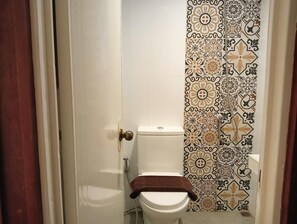 A bathroom with a toilet, a shower curtain with a floral pattern, and a towel on the toilet seat. - Dormitels.ph - El Nido (El Nido)