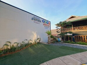 A hotel exterior with a white wall, green lawn, and a signboard advertising 'Suites ECO HOTEL' and 'POPS District El Nido'. - Dormitels.ph - El Nido (El Nido)