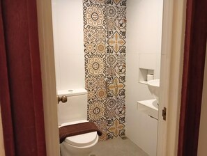 Une petite salle de bain avec des toilettes, un rideau de douche à motifs géométriques et un lavabo blanc avec un miroir au-dessus.