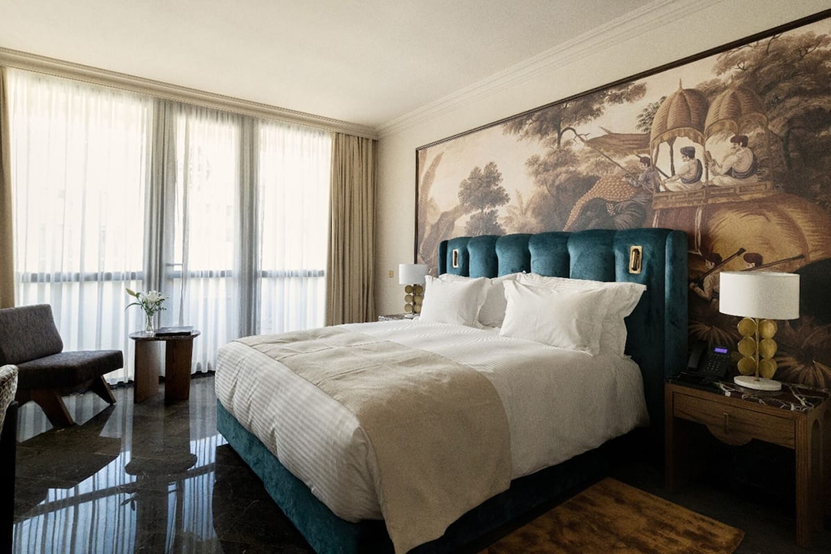 A hotel room with a large bed, a chair, a nightstand, and a large painting on the wall.