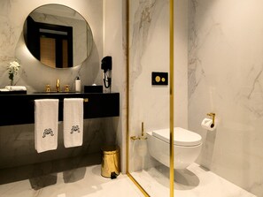 A modern bathroom with a marble sink, two towels, a round mirror, a toilet, and a gold-framed shower enclosure. - Marly Boutique Hotel (Casablanca)