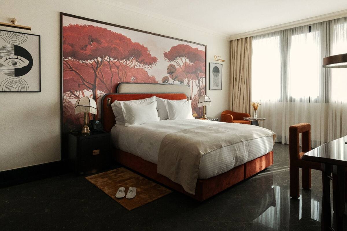 A hotel room with a large bed, a wooden headboard, a nightstand, a desk, and a chair.