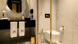 A modern bathroom with a marble sink, two towels, a round mirror, a toilet, and a gold-framed shower enclosure. - Marly Boutique Hotel (Casablanca)