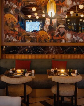 Un restaurante con un mural, mesas redondas y una zona de estar acogedora.