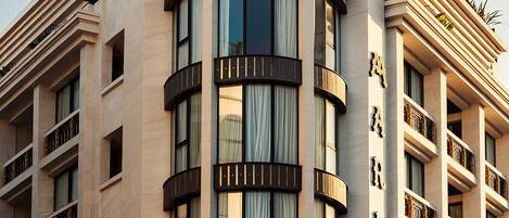 A multi-story hotel with a prominent dome on the top floor, large windows with curtains, and balconies with railings.
