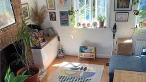 A cozy living room with a fireplace, a blue sofa, and various plants. - Cozy, family-friendly 3-bedroom cottage in Headington (Headington)