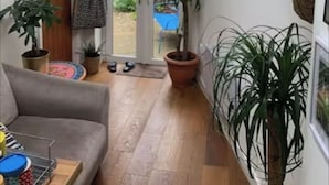 A hallway with a wooden floor, a grey sofa, and several potted plants. - Cozy, family-friendly 3-bedroom cottage in Headington (Headington)