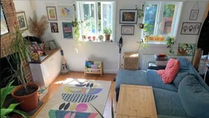 A cozy living room with a blue sofa, a wooden coffee table, and a colorful rug. There are potted plants and artwork on the walls. - Cozy, family-friendly 3-bedroom cottage in Headington (Headington)