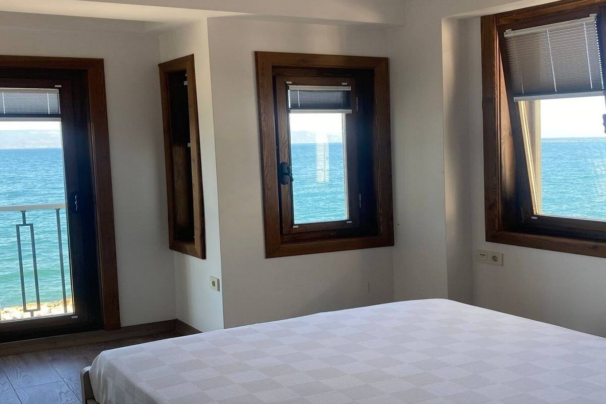 Un dormitorio con cama, vista al mar a través de una puerta de balcón y ventana con vistas al mar.