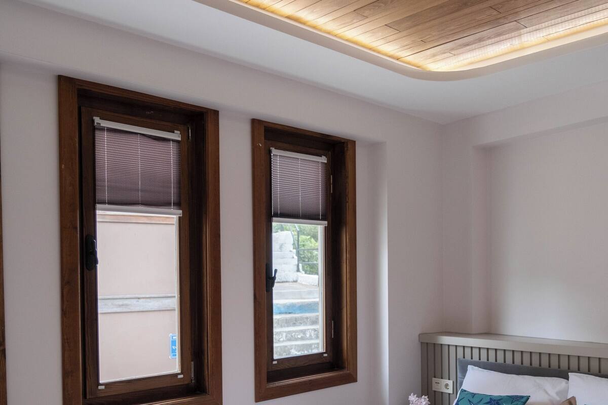 Un dormitorio con una cama, dos ventanas con persianas, una lámpara de techo y un radiador.