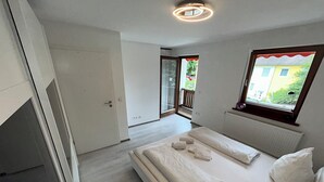A modern bedroom with a large bed, a view of the outside, and a sliding glass door leading to a balcony. - Cozy terraced house for up to 8 people1 minute from the trade fair (Offenburg)