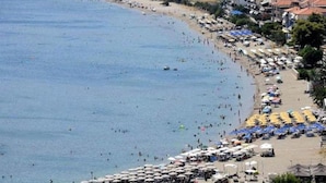 Une plage côtière bordée de nombreux parasols et de chaises longues, ce qui indique la présence d’une zone de villégiature balnéaire.