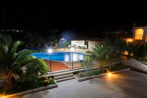 A nighttime view of a swimming pool area with a covered seating area and a stone building in the background.