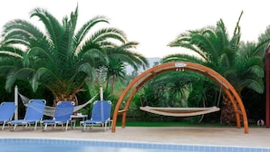 Un espace aménagé au bord de la piscine, avec un fauteuil suspendu, des chaises longues et des palmiers.