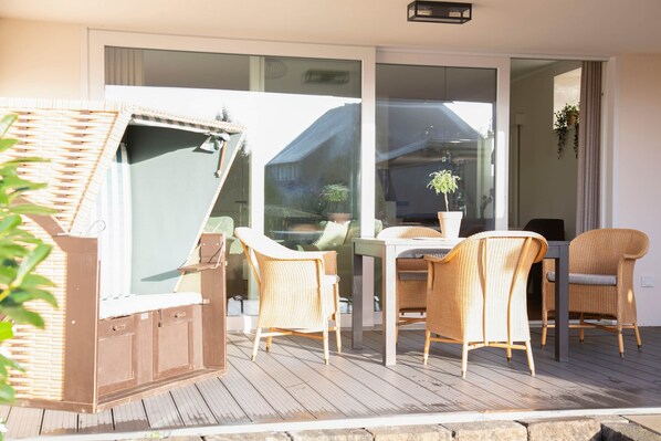 Une terrasse en bois avec des meubles en osier, une porte vitrée donnant sur un balcon et une plante en pot.