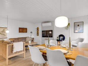 Et moderne spiseområde med et træbord, hvide stole og et fjernsyn monteret på væggen.
