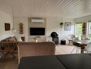 A modern living room with a flat-screen TV, a fireplace, a dining area with a table and chairs, and a large window providing natural light. - "Nicklas" - 250m from the sea by Interhome (Sydals)