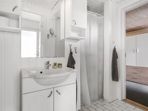 A modern bathroom with a white vanity, a large mirror, a shower curtain, and a towel hanging on the wall.