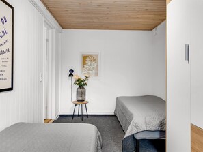 A bedroom with two beds, a small table with a vase, and a framed picture on the wall.
