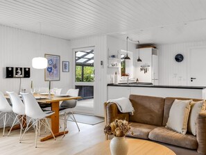 Ett modernt kök med vita köksskåp, en matplats med vita stolar och en brun soffa.