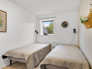 Ett rum med två separata sängar, ett fönster med utsikt över träd, en uggleliknande dekoration som hänger på väggen och en flätad korg med en blomma i.