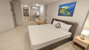 Una habitación de hotel con cama, mesita de noche, un cuadro, sofá y televisor.