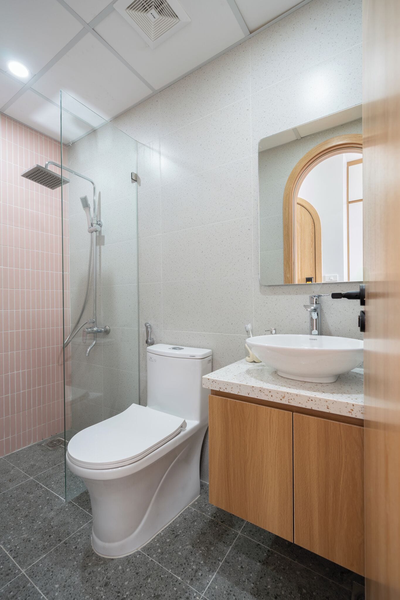 A modern bathroom with a glass-enclosed shower, a white toilet, and a wooden vanity with a sink.