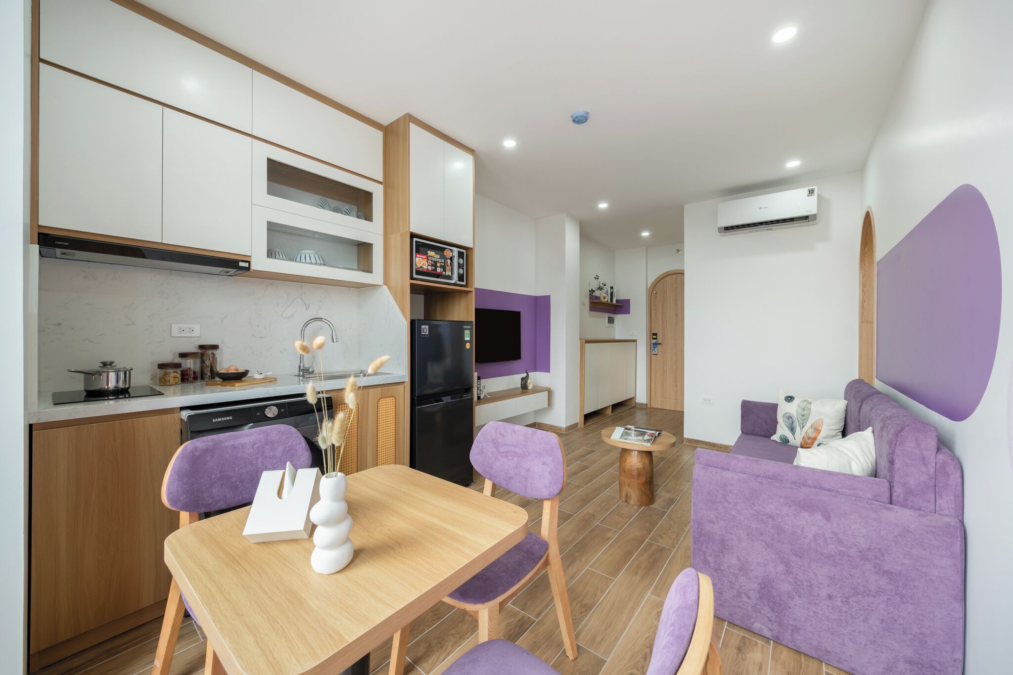 A modern kitchen with white cabinets, a black refrigerator, and a dining area with a wooden table and purple chairs.