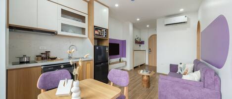 A modern kitchen with white cabinets, a black refrigerator, and a dining area with a wooden table and purple chairs.