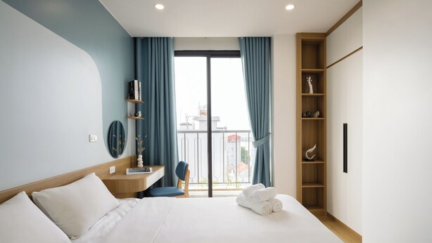 Quarto de hotel moderno com uma cama grande, uma escrivaninha e vista para a cidade pela janela.