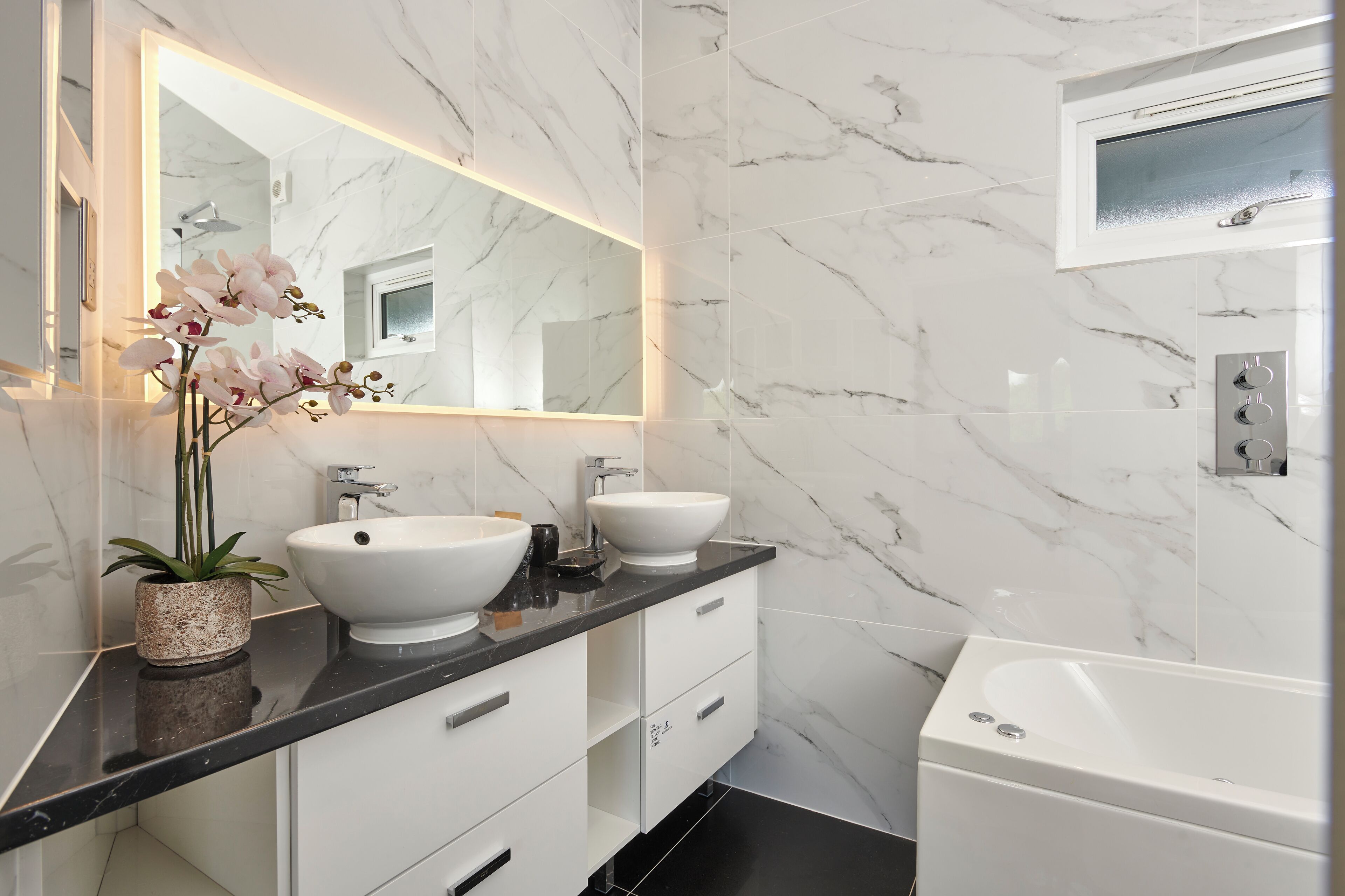 A modern bathroom with a marble backsplash, two sinks, a large mirror, and a bathtub.
