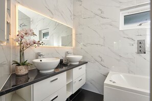 Une salle de bain moderne avec un pare-baignoire en marbre, deux vasques, un grand miroir et une baignoire.