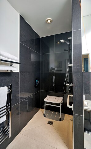 A modern bathroom with dark tiles, a shower, a small bench, and a towel rack. -  Lakehurst Park (Milton Keynes)