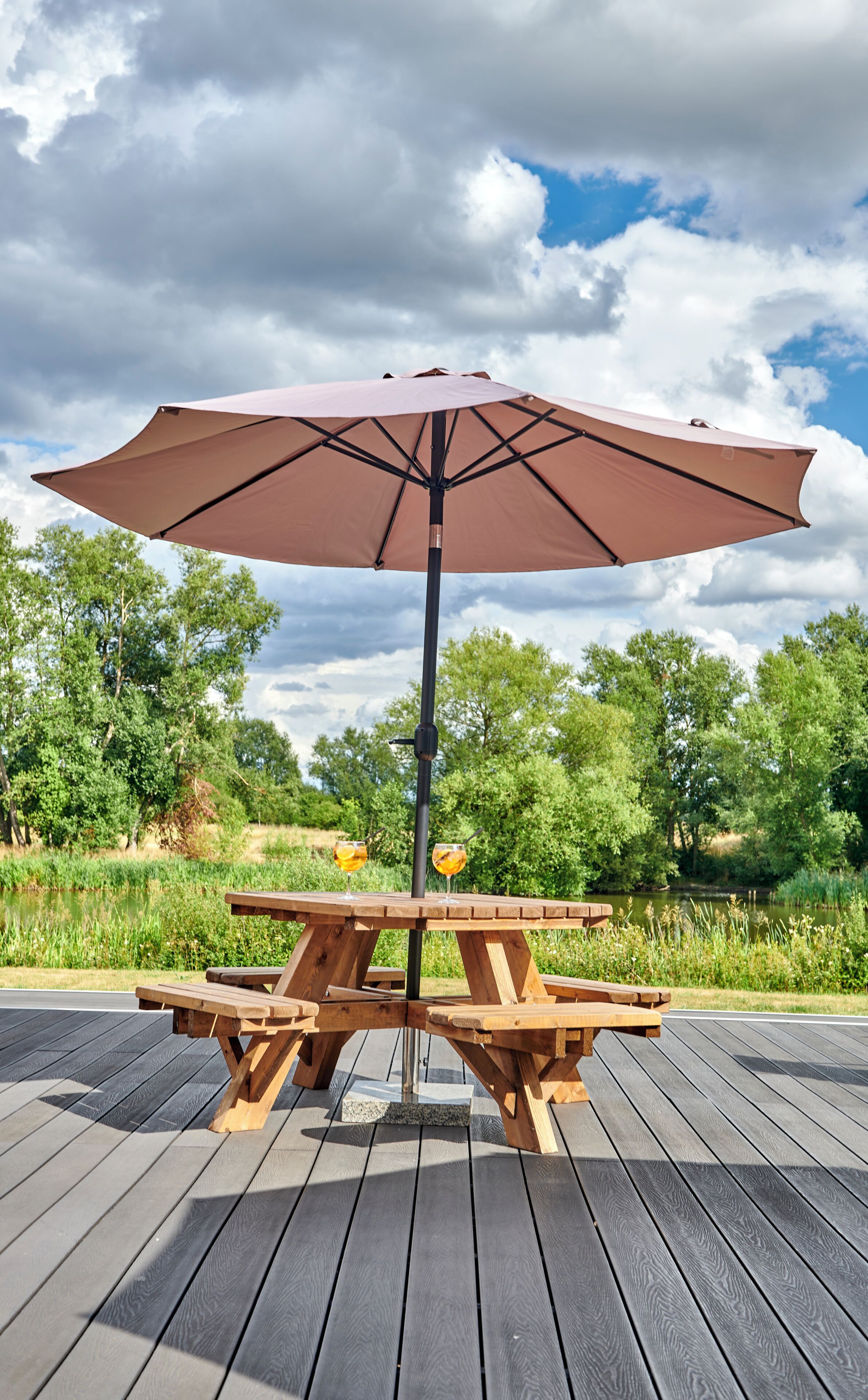 A wooden picnic table with an umbrella, surrounded by a wooden deck and greenery.