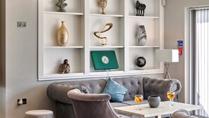A modern living room with a grey sofa, two armchairs, a coffee table, and decorative shelves with various items.