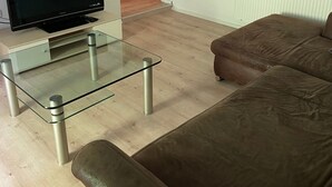 A living room with a glass coffee table, a brown leather sofa, a flat-screen TV, and a white radiator. - Entire Apartment in a Quiet Location (Oerlenbach)