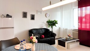 A modern living room with a dining table, black leather sofa, and a small side table with a vase of flowers.